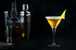 Sidecar cocktail with cognac, liqueur, lemon juice and ice. Black background, bar tools, copy space